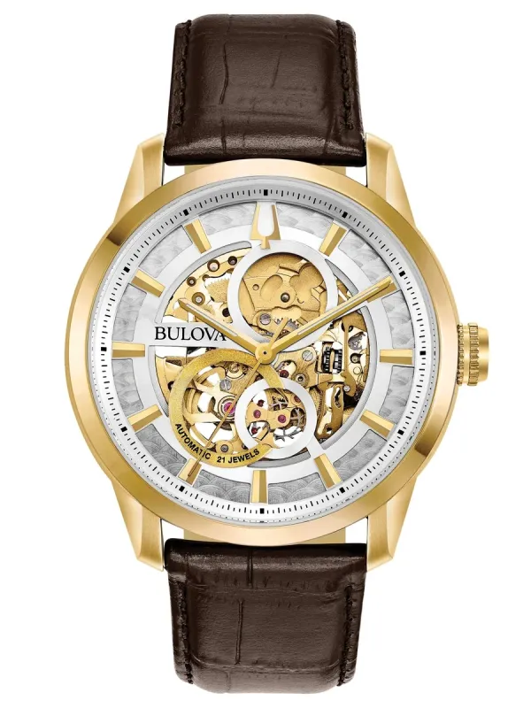 Vista frontal del reloj con esfera skeleton, caja dorada y correa de piel marrón sobre fondo blanco.