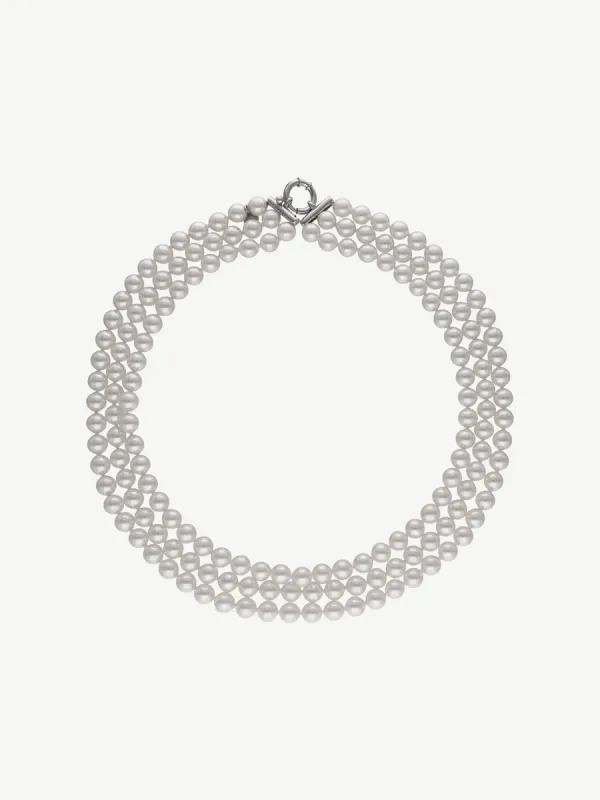 Collar de tres vueltas de perlas blancas dispuesto en círculo sobre fondo blanco, vista cenital.