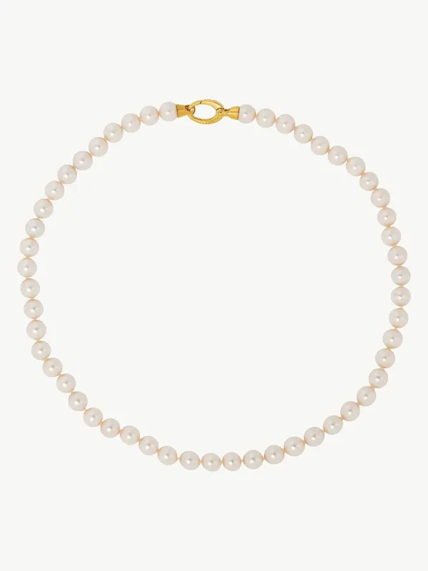 Collar de perlas dispuesto en círculo sobre fondo blanco, vista cenital con detalle del cierre dorado.
