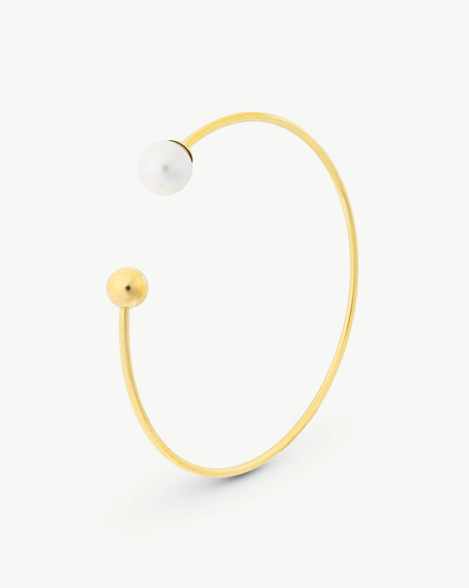 Bracelet jonc doré vu de profil, avec une perle blanche et un terminal sphérique sur fond blanc.