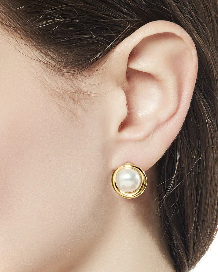 Gros plan latéral d'une boucle d'oreille en perle dorée portée à l'oreille, fond flou.