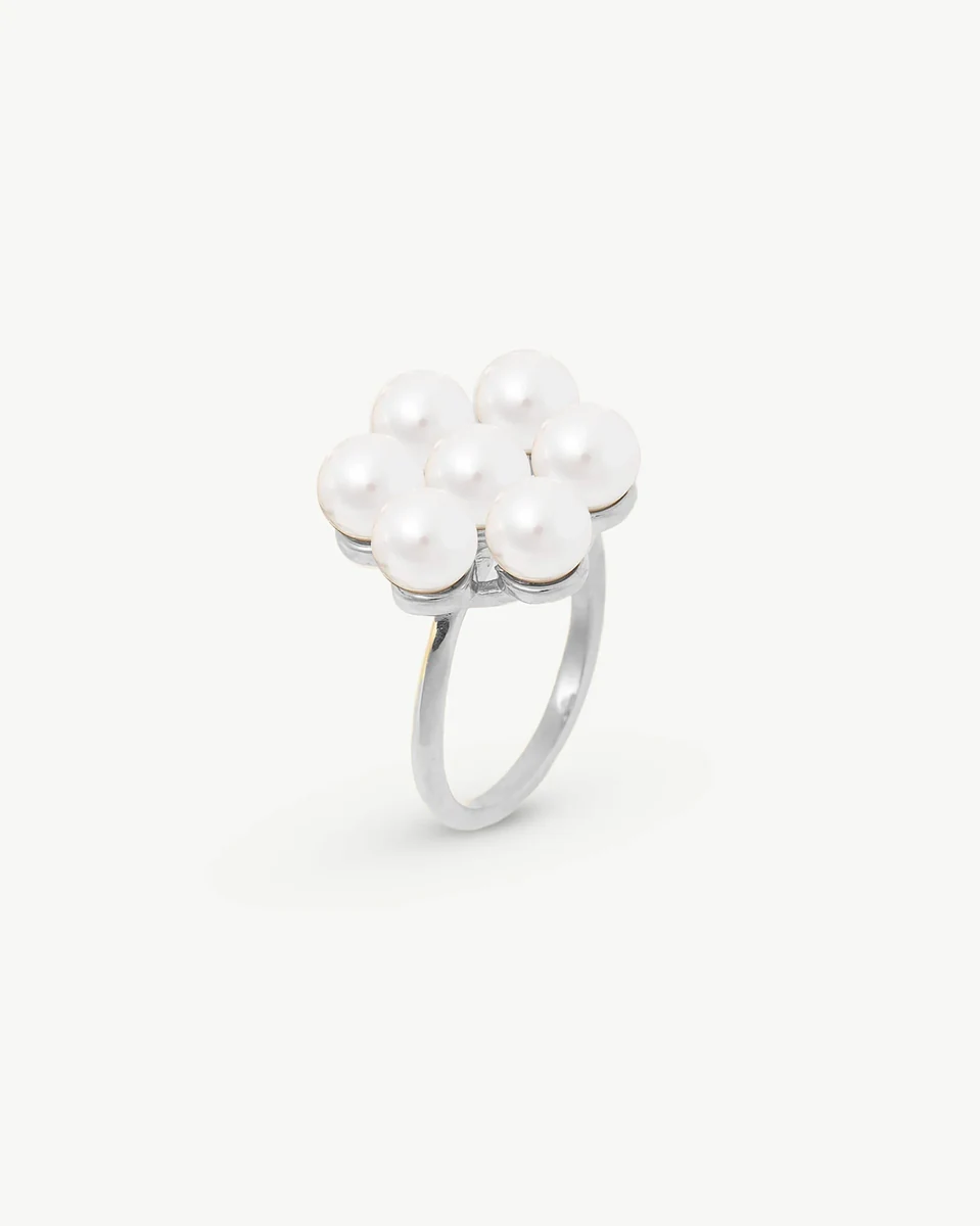 Anillo de perlas en forma de flor visto desde un ángulo lateral, sobre fondo blanco.