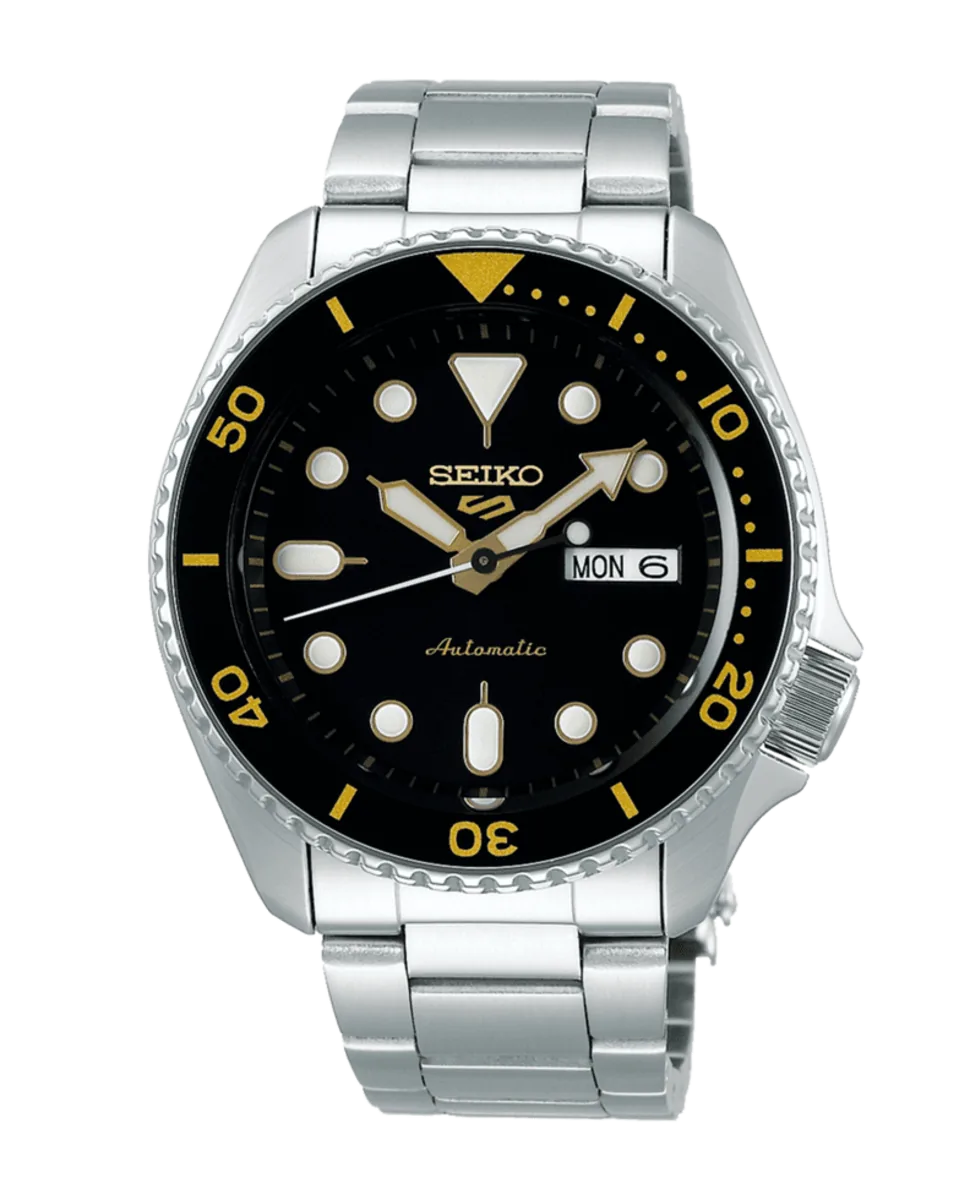 Vista frontal del reloj con esfera negra y detalles dorados, brazalete de acero inoxidable, fondo blanco.