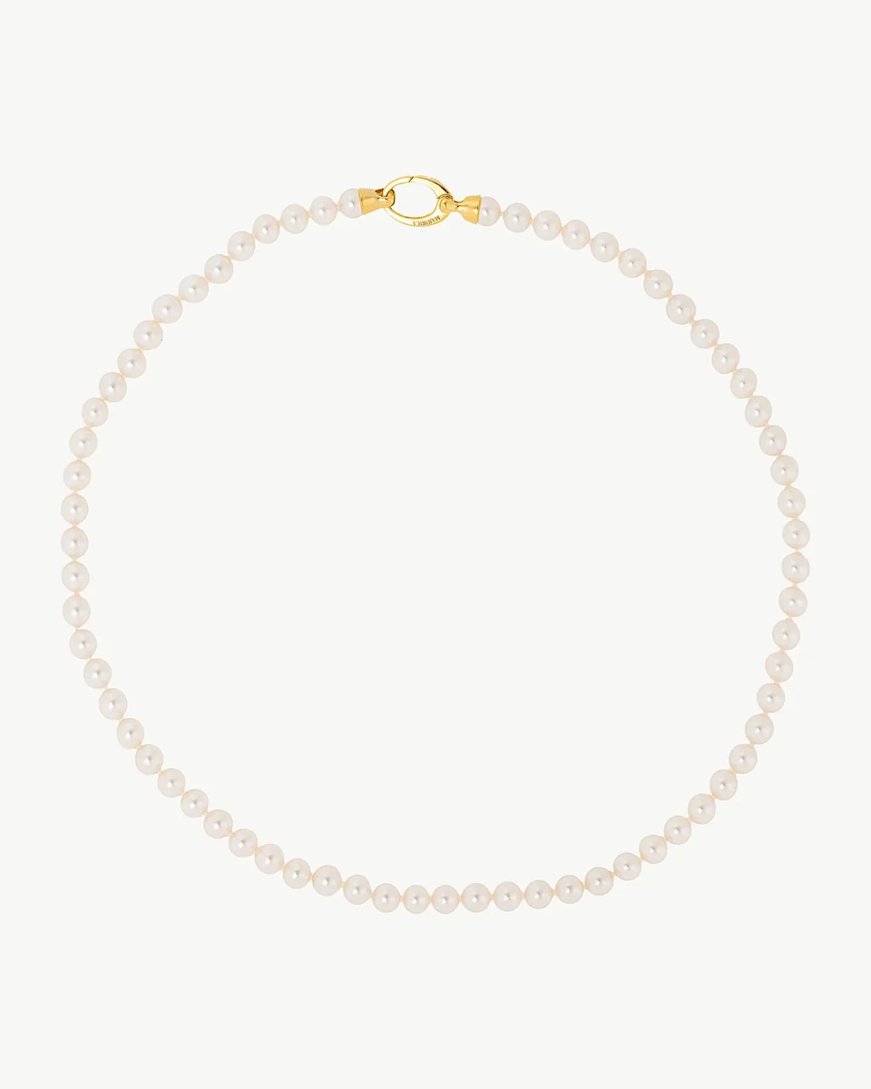 Collar de perlas dispuesto en círculo sobre fondo blanco, vista cenital con el cierre dorado en la parte superior.