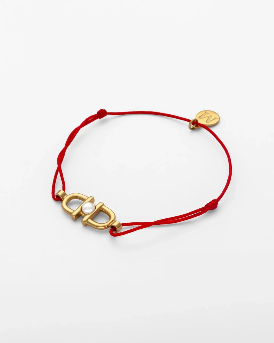 Rotes Cordarmband mit goldenem Steigbügel-Anhänger und Perle, Frontansicht auf weißem Hintergrund.