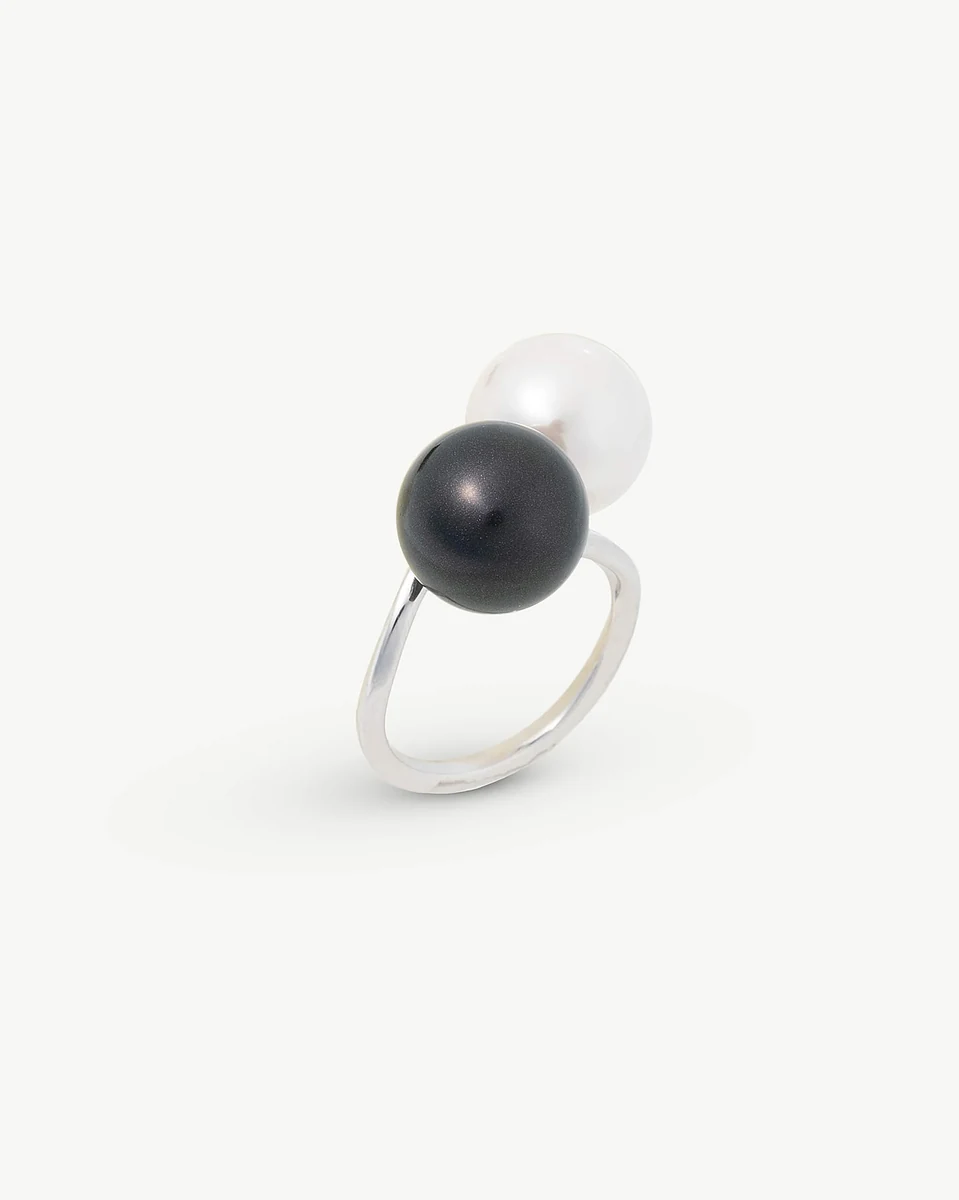 Bague en argent avec perles blanche et noire, vue de profil, sur fond blanc.
