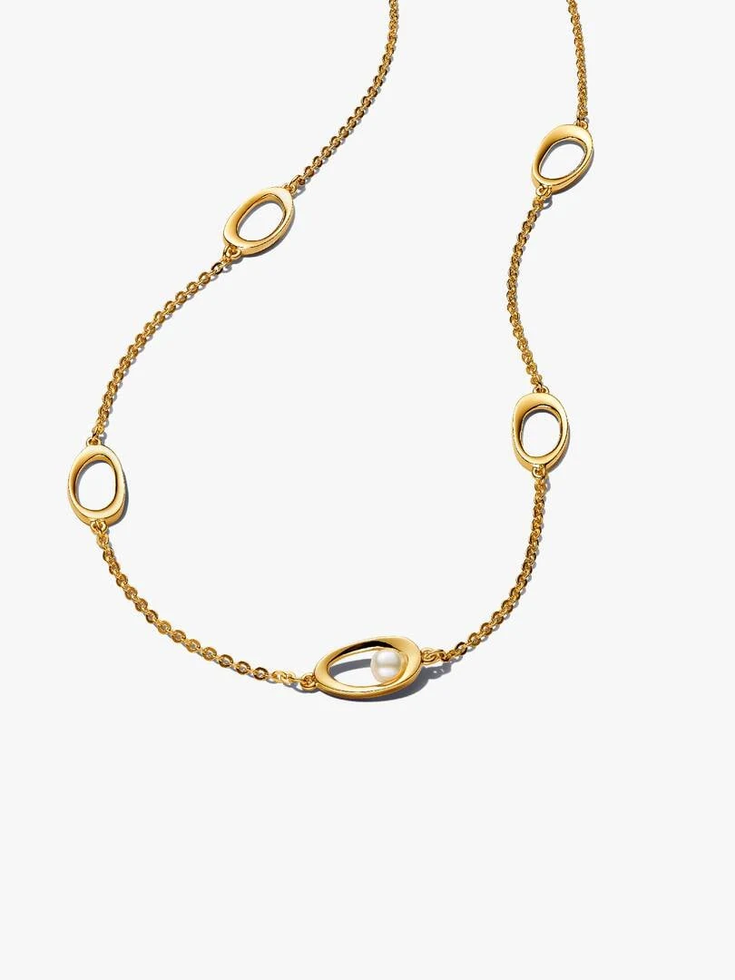Gold necklace with organic oval links and a white pearl, top-down view on a white background.