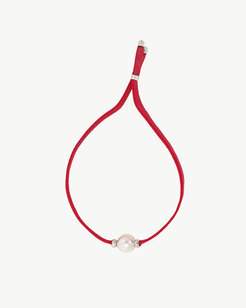 Front view of the bracelet on a white background, showing the coral red cord and central white pearl.