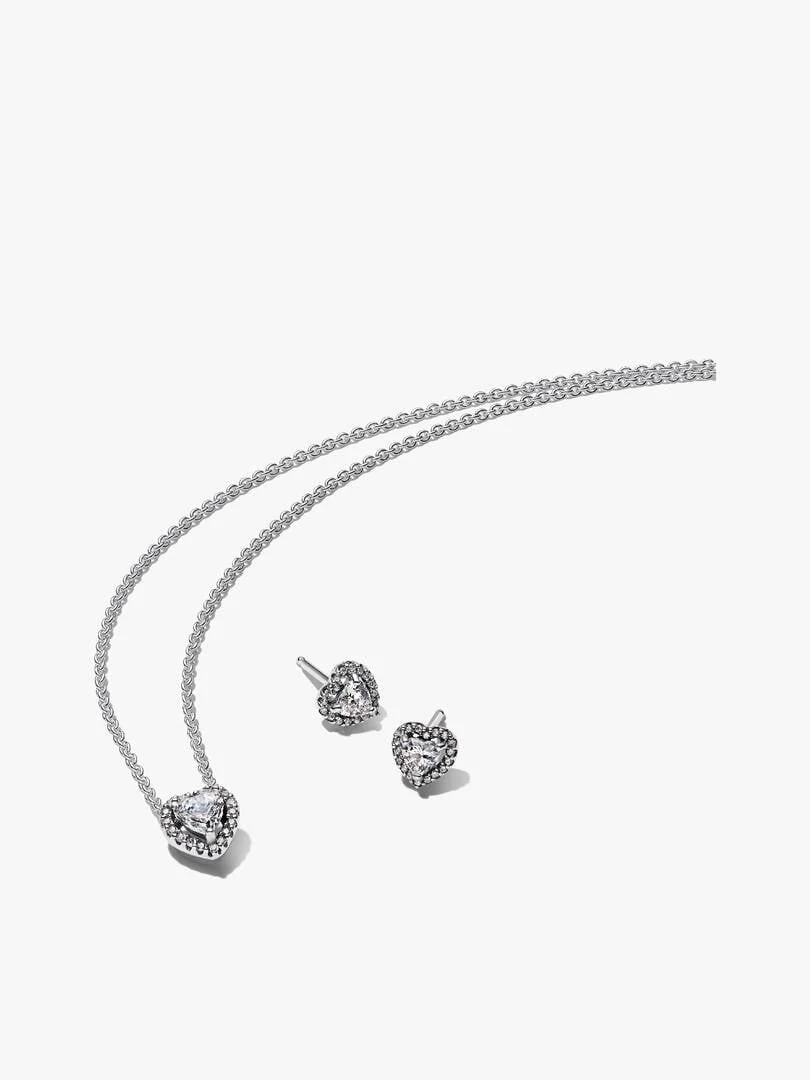 Collar y pendientes de corazón en plata sobre fondo blanco, vista frontal con cadena extendida.