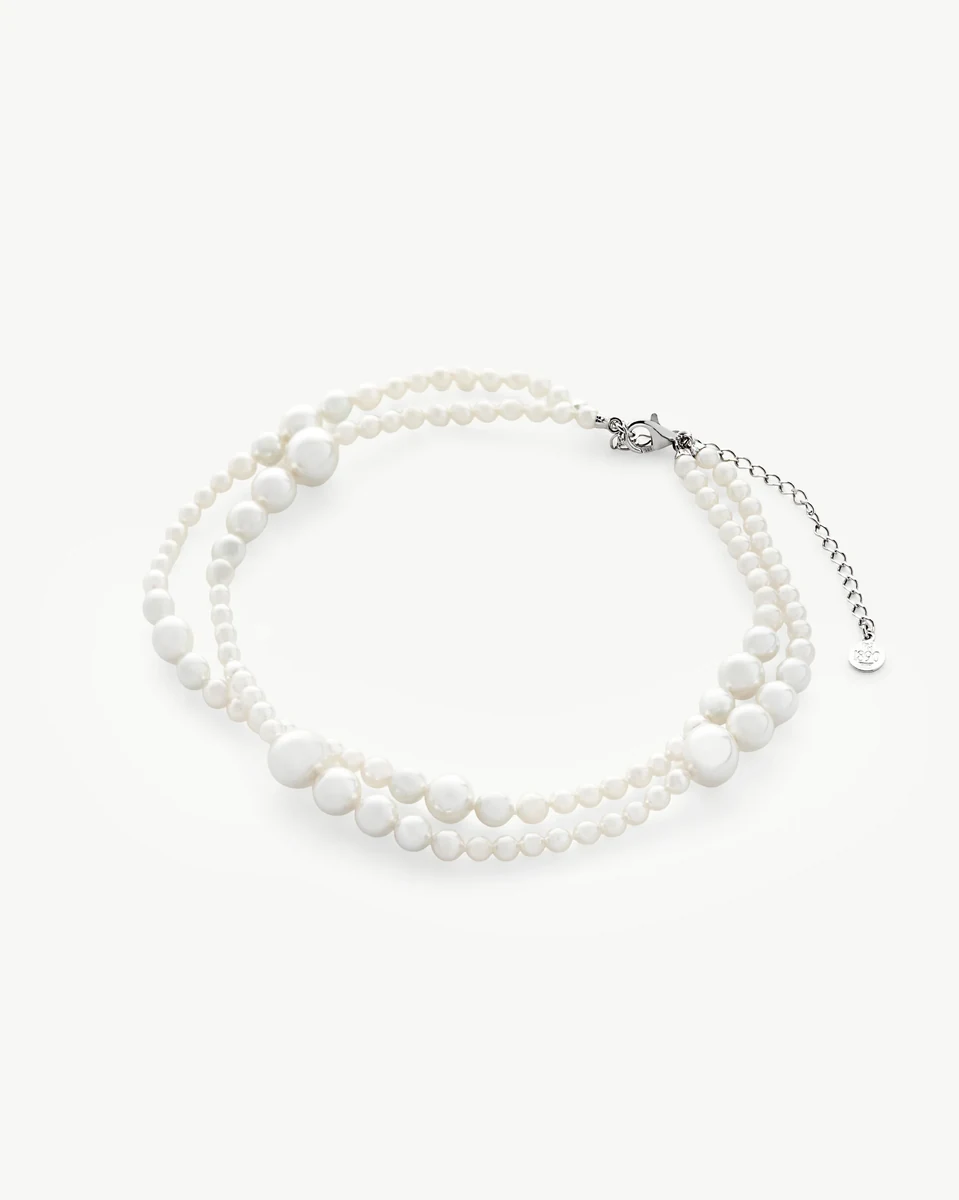 Double strand white pearl necklace arranged in a circle on a white background, top view.