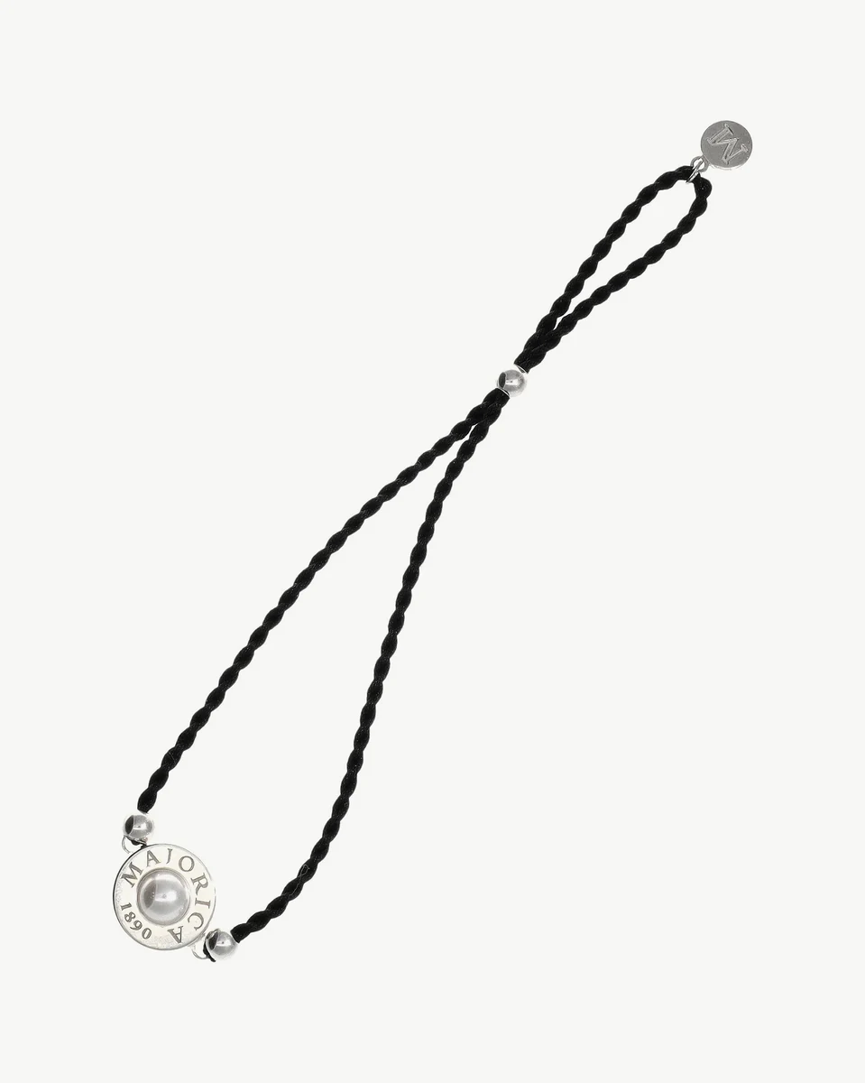 Black braided bracelet with central pearl and circular clasp, top view on white background.