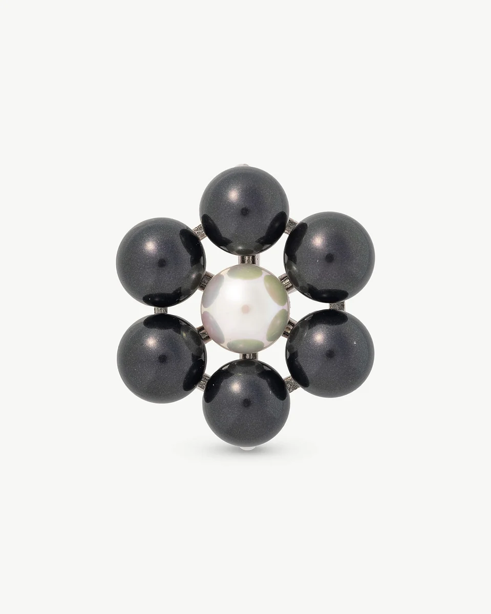 Vista frontal de broche floral con perlas negras y blanca central, fondo blanco puro.