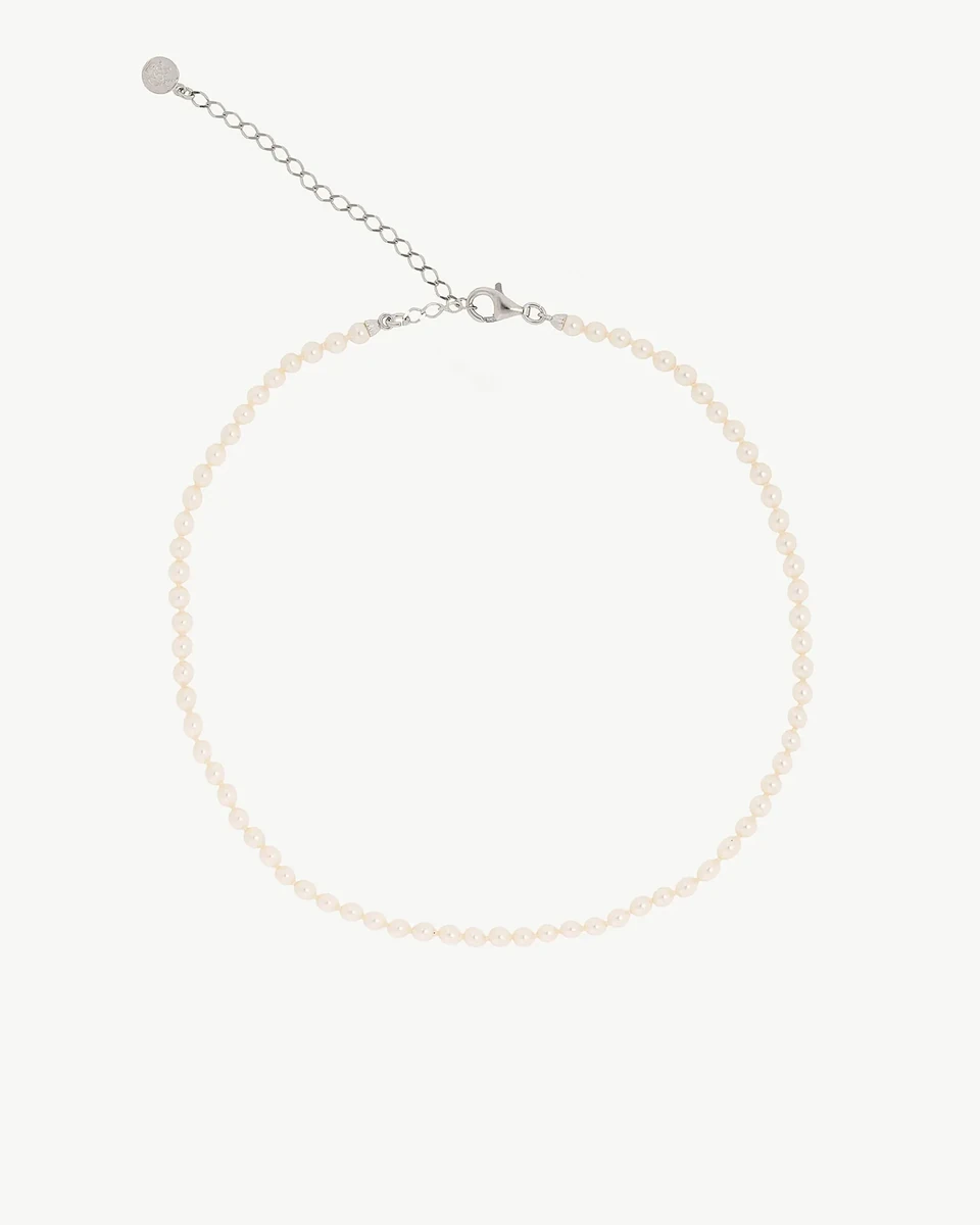 Collar de perlas dispuesto en círculo sobre fondo blanco, vista cenital con detalle del cierre y cadena extensora.