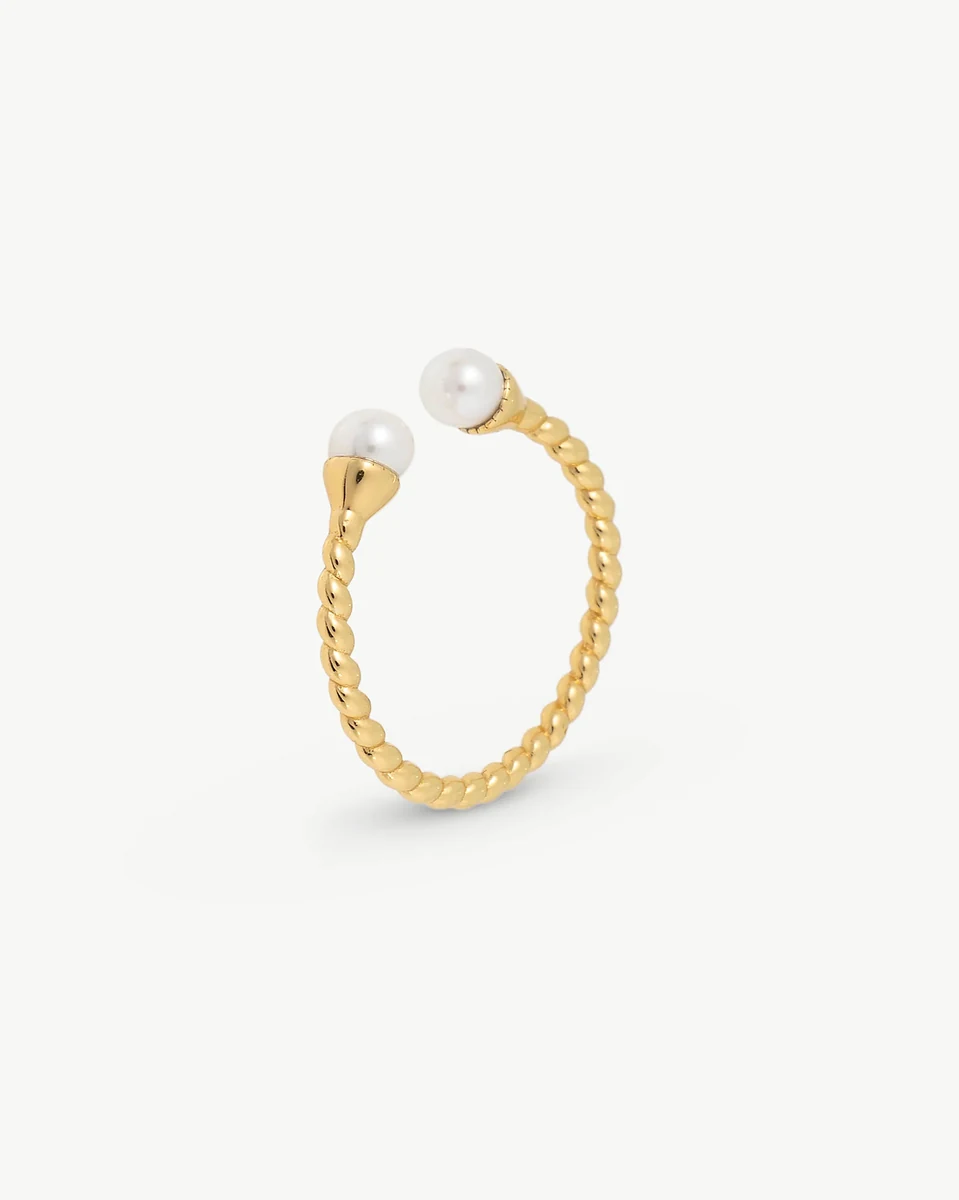 Anillo de diseño trenzado con dos perlas blancas, vista lateral en ángulo sobre fondo blanco.