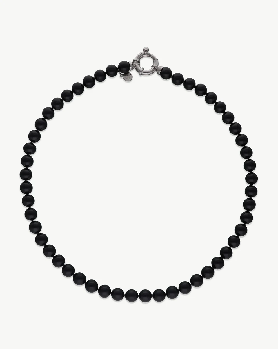 Collier de perles noires disposé en cercle sur fond blanc, vue de face avec fermoir en argent visible.