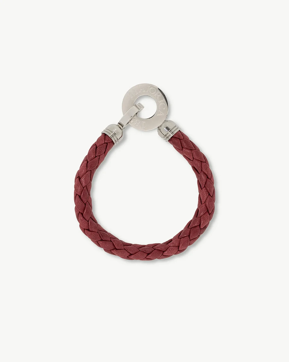 Pulsera de cuero trenzado rojo vista desde arriba, con cierre circular de acero grabado, fondo blanco.