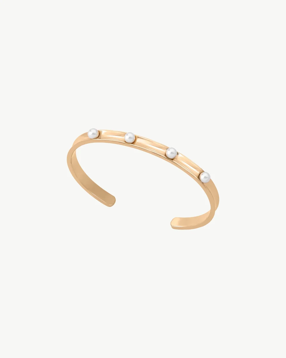 Gold rigid bangle with white pearls, side angle view on a white background.