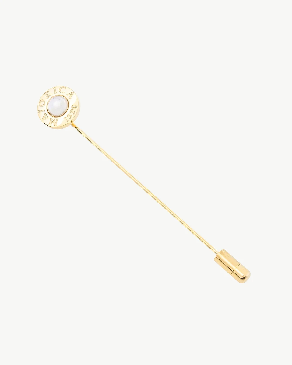 Épingle dorée vue en angle diagonal sur fond blanc, avec une perle blanche centrale et logo gravé.