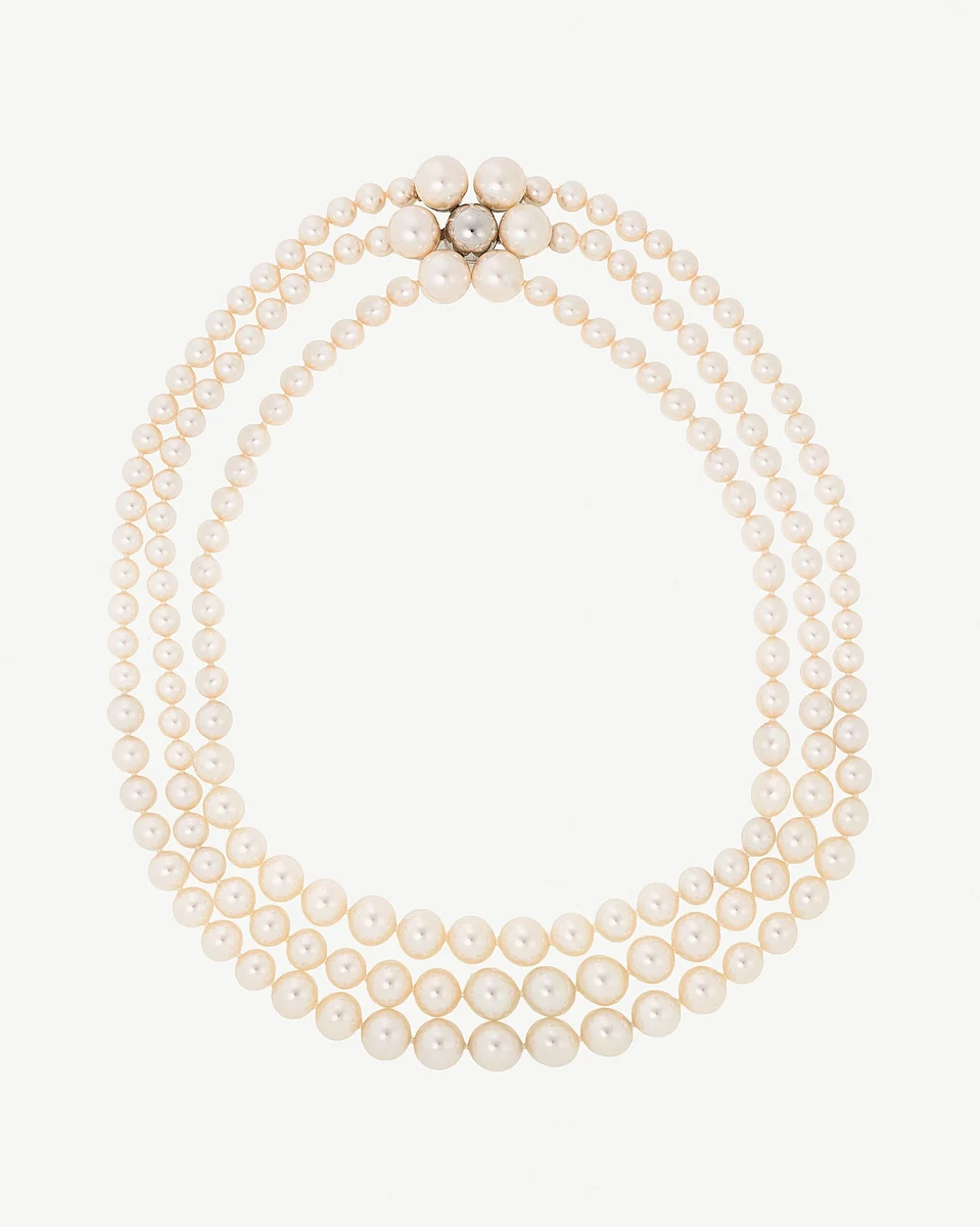 Three-strand white pearl necklace on a white background, front view featuring a central floral clasp.