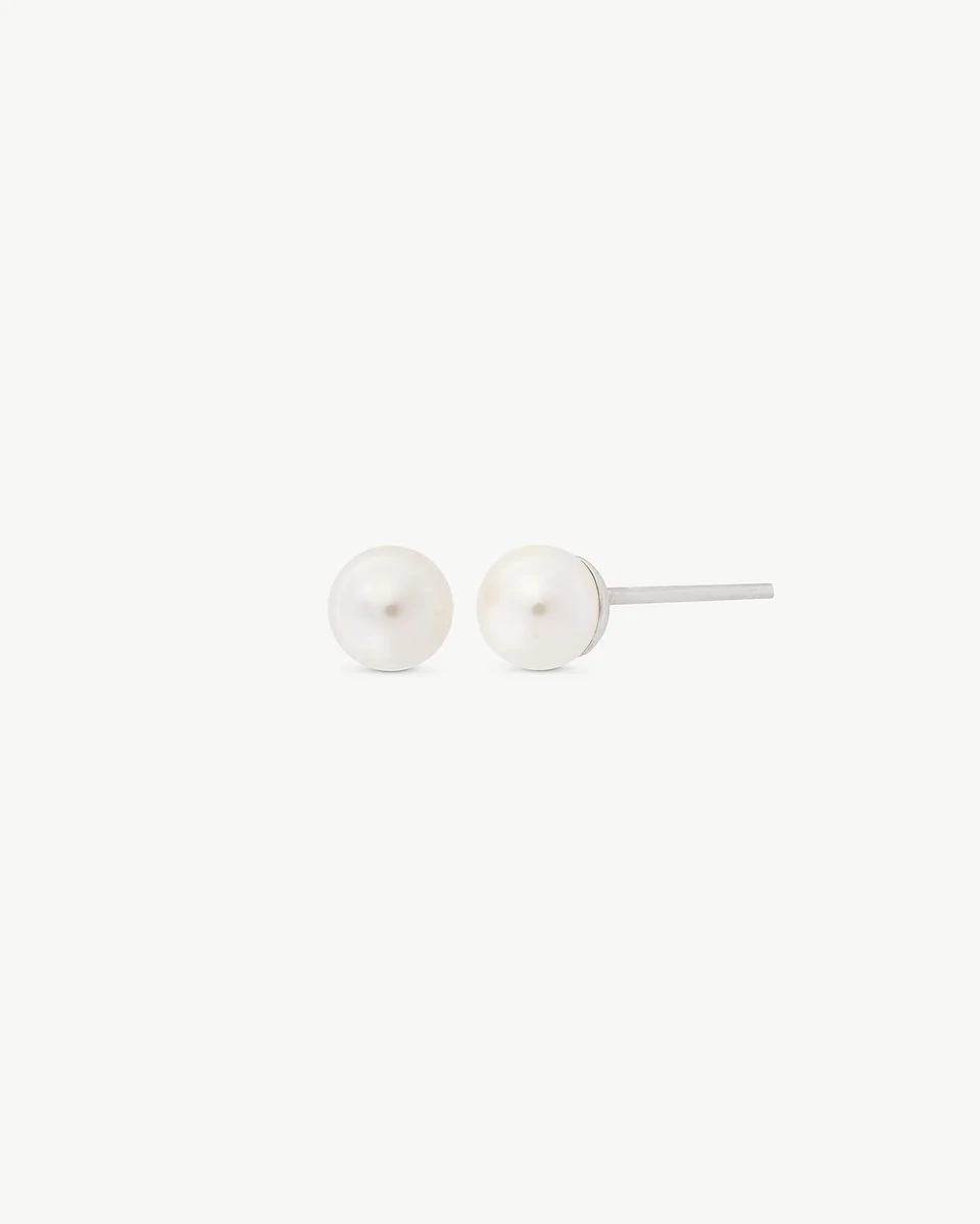Pendientes de perla blanca sobre fondo blanco, vista frontal y lateral con detalle del cierre de pincho.