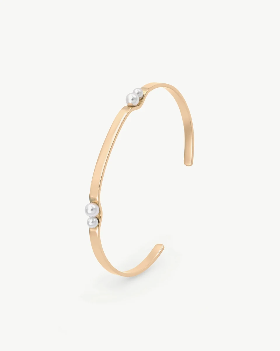 Gold rigid bangle with white pearls, side angle view on a white background.