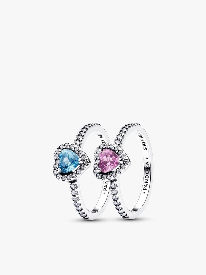 Vista frontal de dos anillos con cristales en forma de corazón azul y lila, fondo blanco.