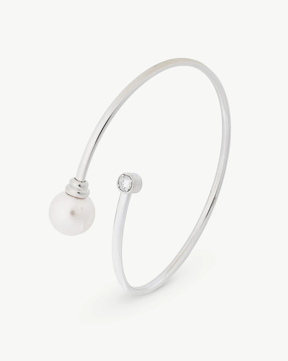 Brazalete rígido de plata visto en ángulo lateral sobre fondo blanco, destacando la perla y la circonita.