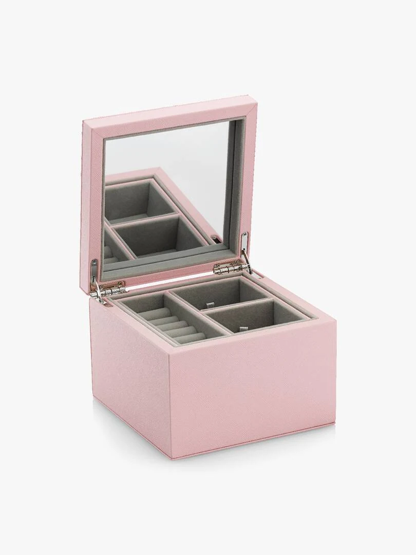 Coffret à bijoux rose ouvert de trois quarts, montrant les compartiments et le miroir du couvercle, fond blanc.