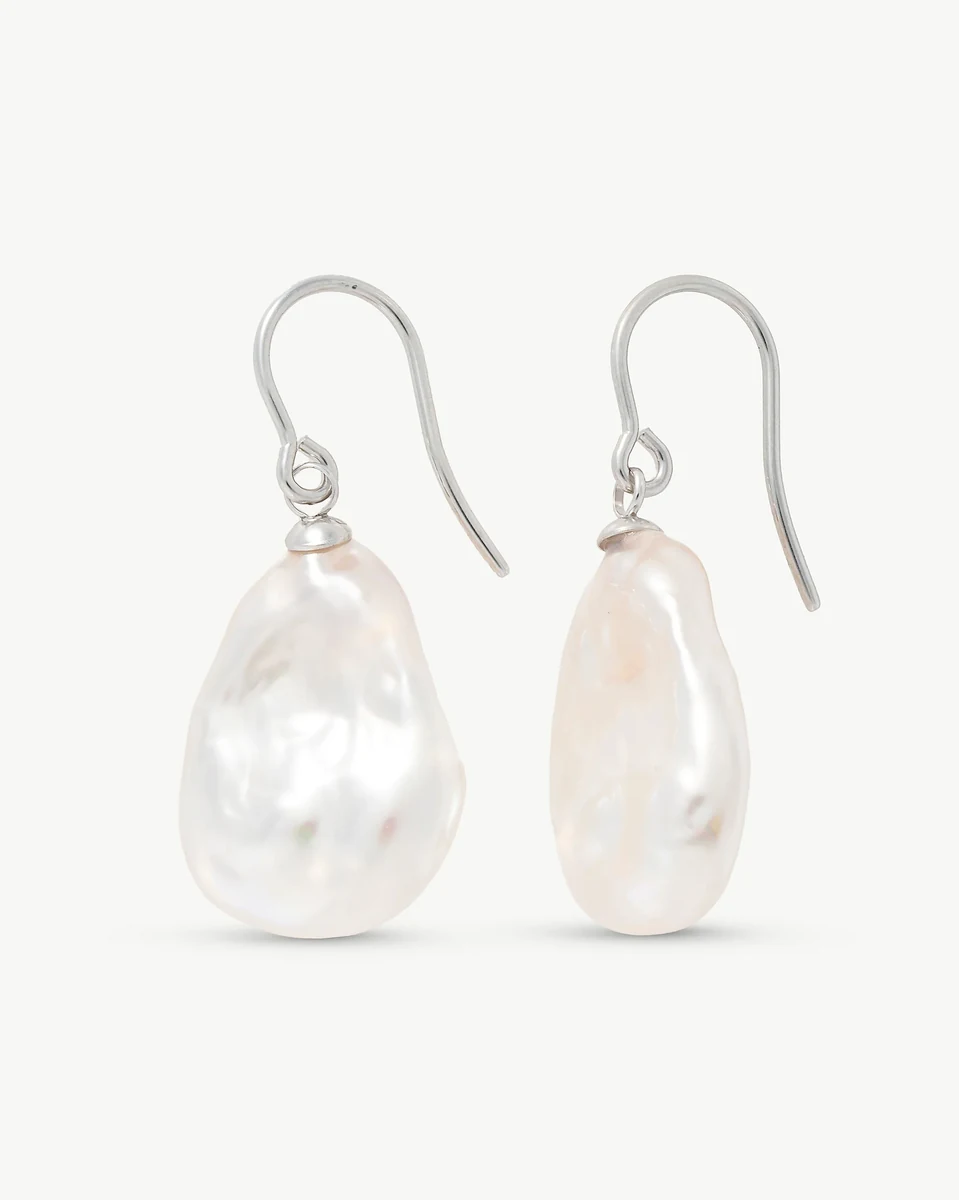 Vue de face des boucles d'oreilles en perles baroques blanches avec crochets en argent sur fond blanc.