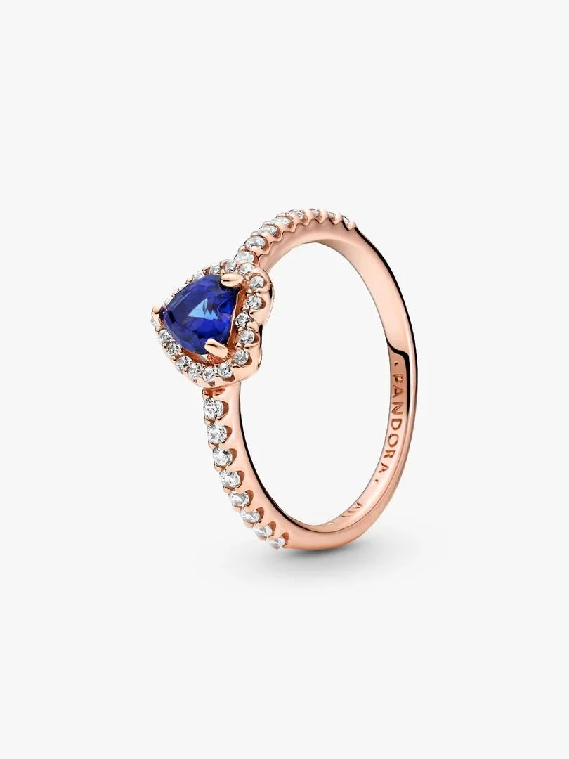 Rose gold ring with blue heart-shaped gem, angled side view on a white background.