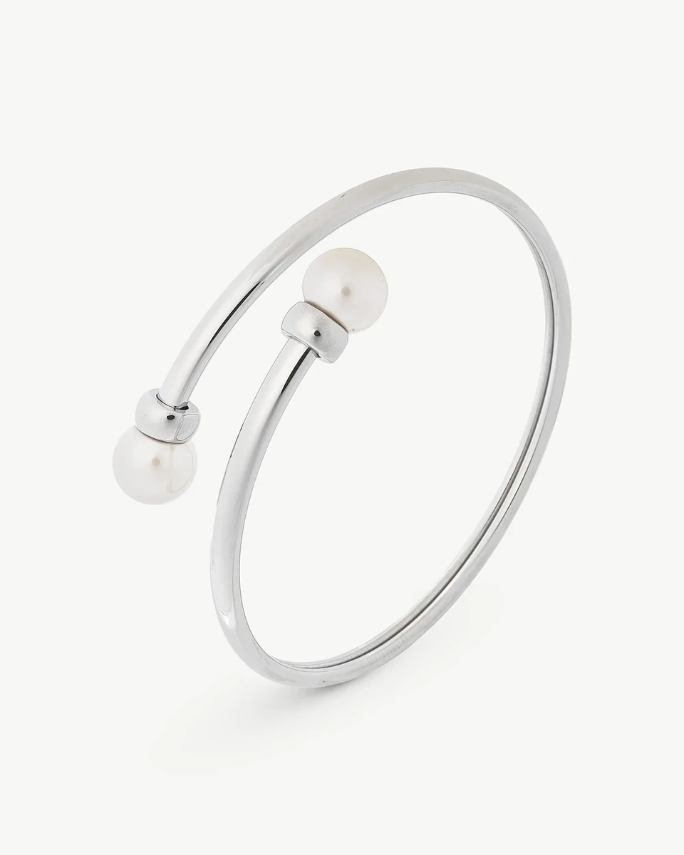 Brazalete rígido de acero con dos perlas blancas en los extremos, vista en ángulo sobre fondo blanco.