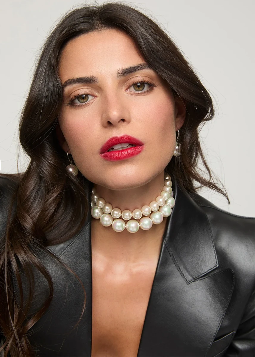 Close-up of model wearing double-strand white pearl necklace and matching earrings, neutral background.