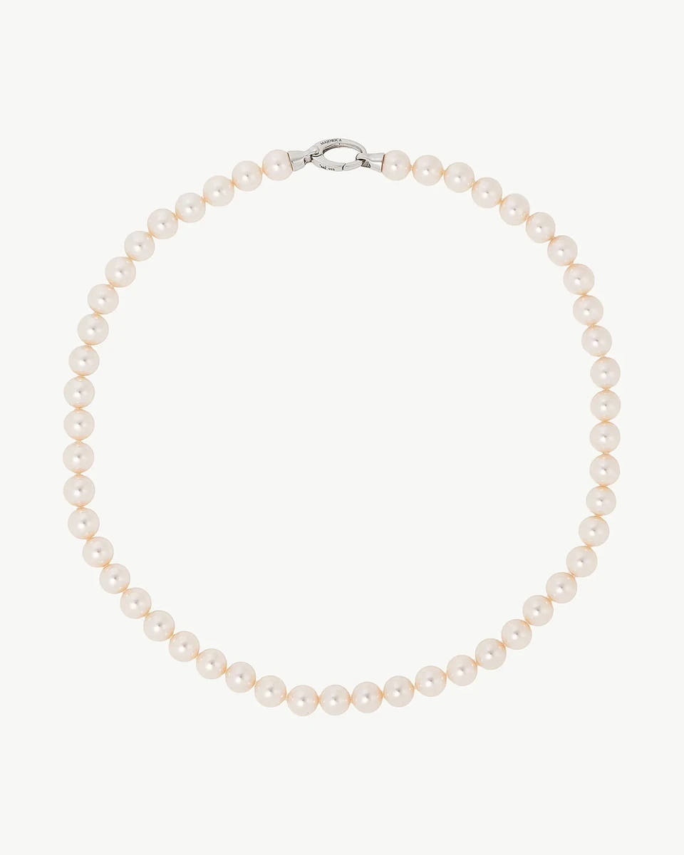 Collar de perlas dispuesto en círculo sobre fondo blanco, vista cenital con detalle del cierre superior.