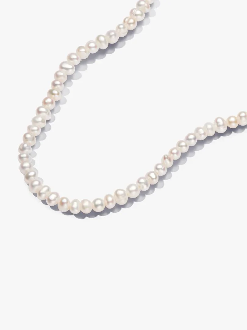 White pearl necklace arranged in a curve on a white background, top-down view.