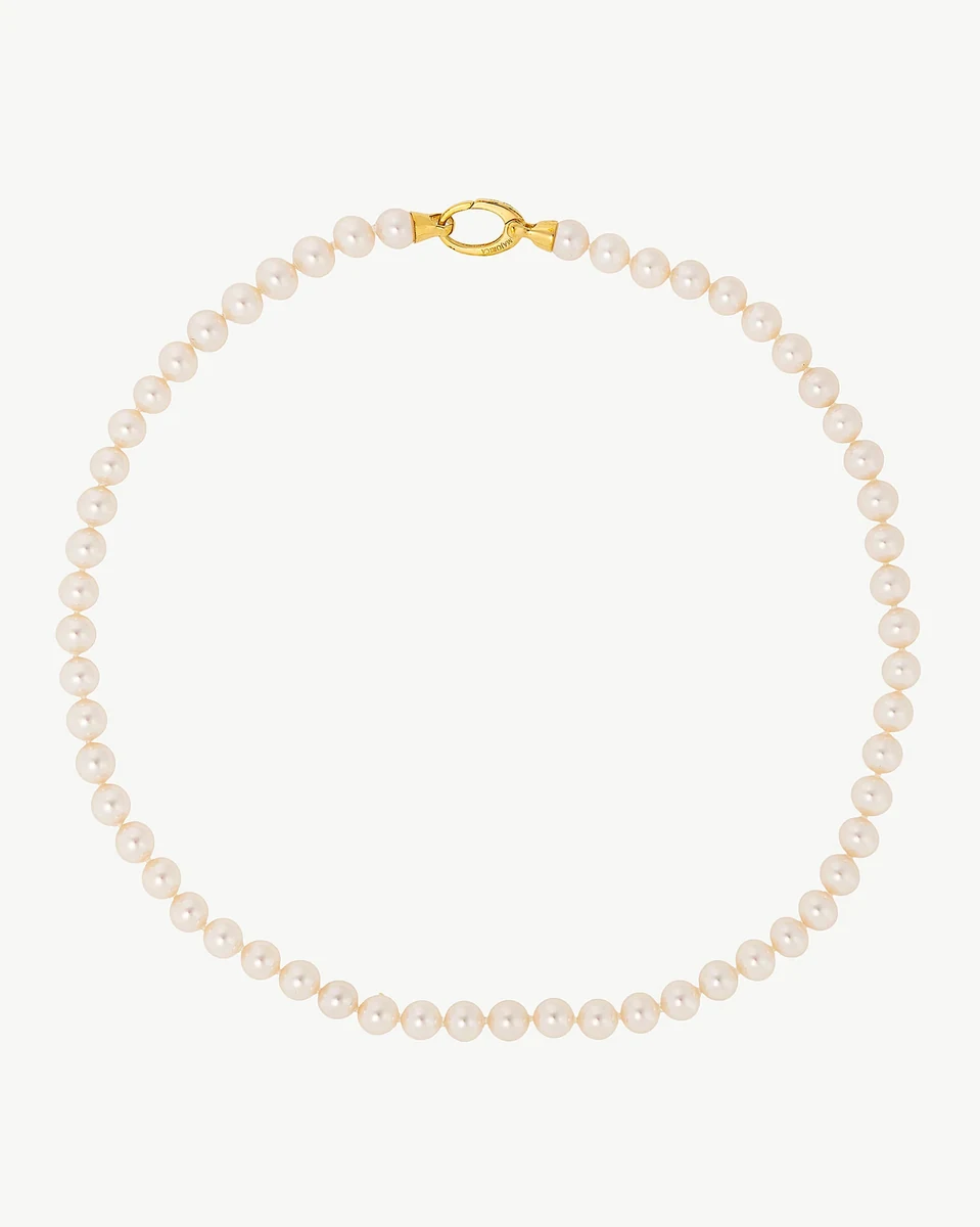 Collier de perles disposé en cercle sur fond blanc, vue de face avec le fermoir doré visible.