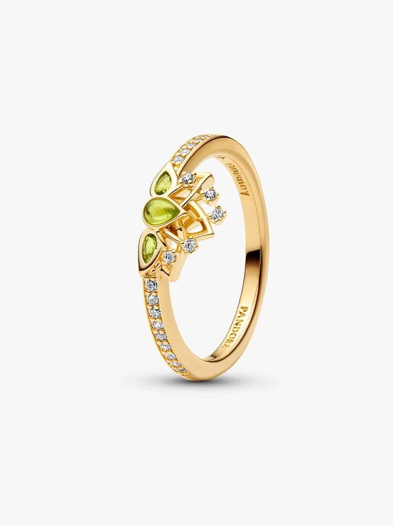 Anillo de tiara visto en ángulo lateral, fondo blanco, detalle de gemas verdes y brillantes sobre banda dorada.