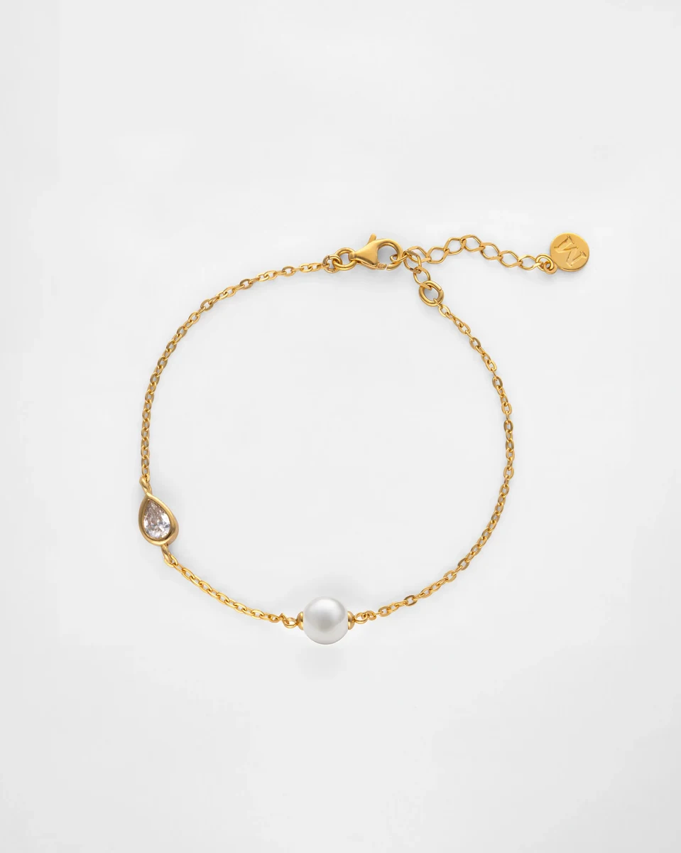 Draufsicht auf goldene Gliederkette mit weißer Perle und Zirkonia auf weißem Hintergrund.