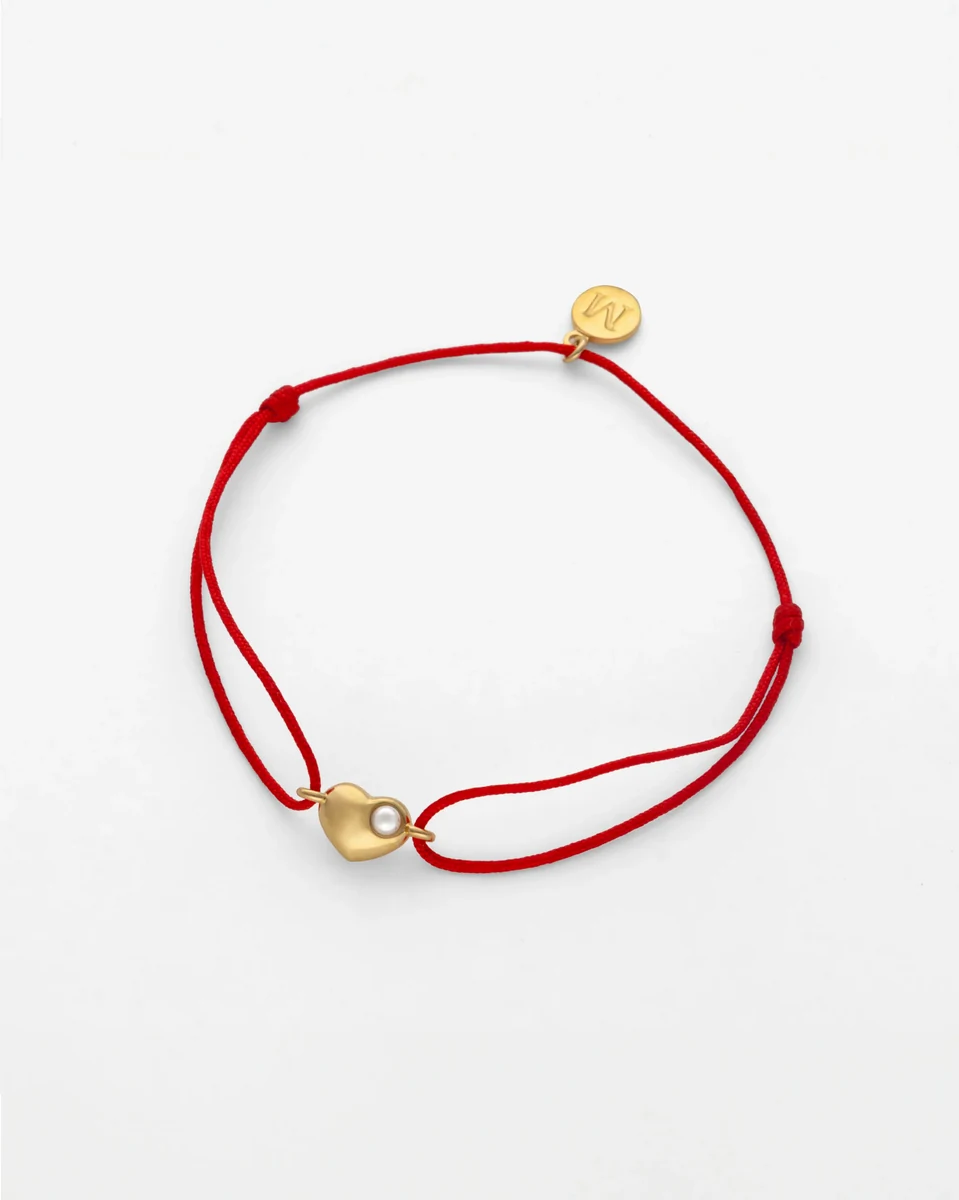 Vue de dessus du bracelet en cordon rouge avec pendentif cœur doré et perle, sur fond blanc.