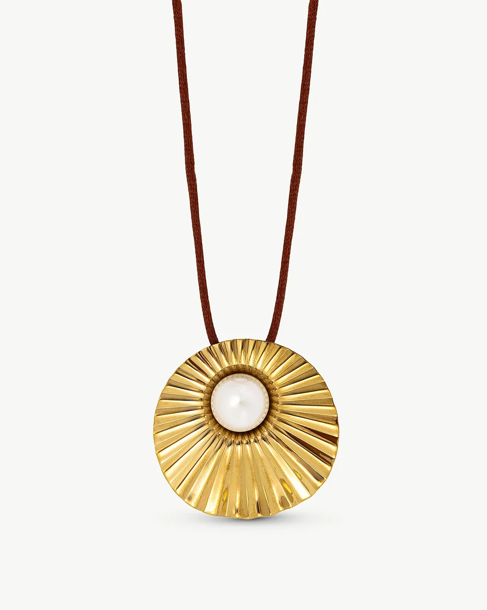 Pendentif circulaire doré strié avec perle centrale sur cordon marron, vue de face, fond blanc.