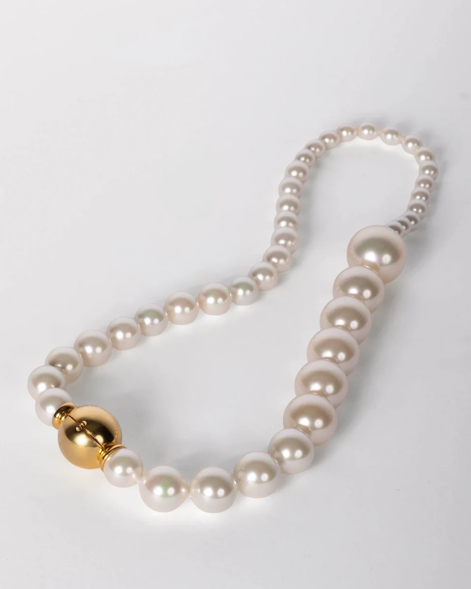 Collier de perles blanches disposé en courbe sur fond blanc, vue de dessus avec focus sur le fermoir doré.
