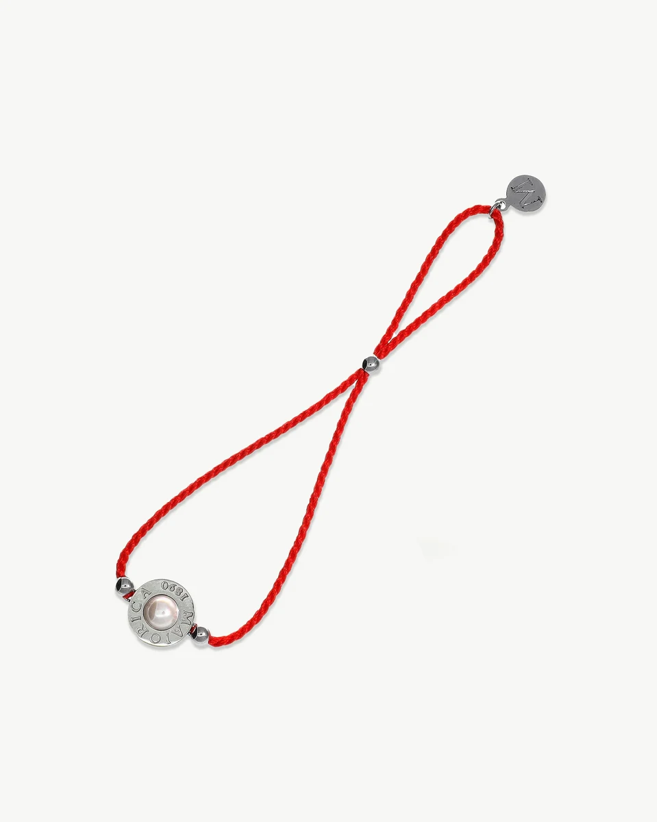Red braided bracelet viewed from a top angle, white background, detail of the pearl and metal clasp.