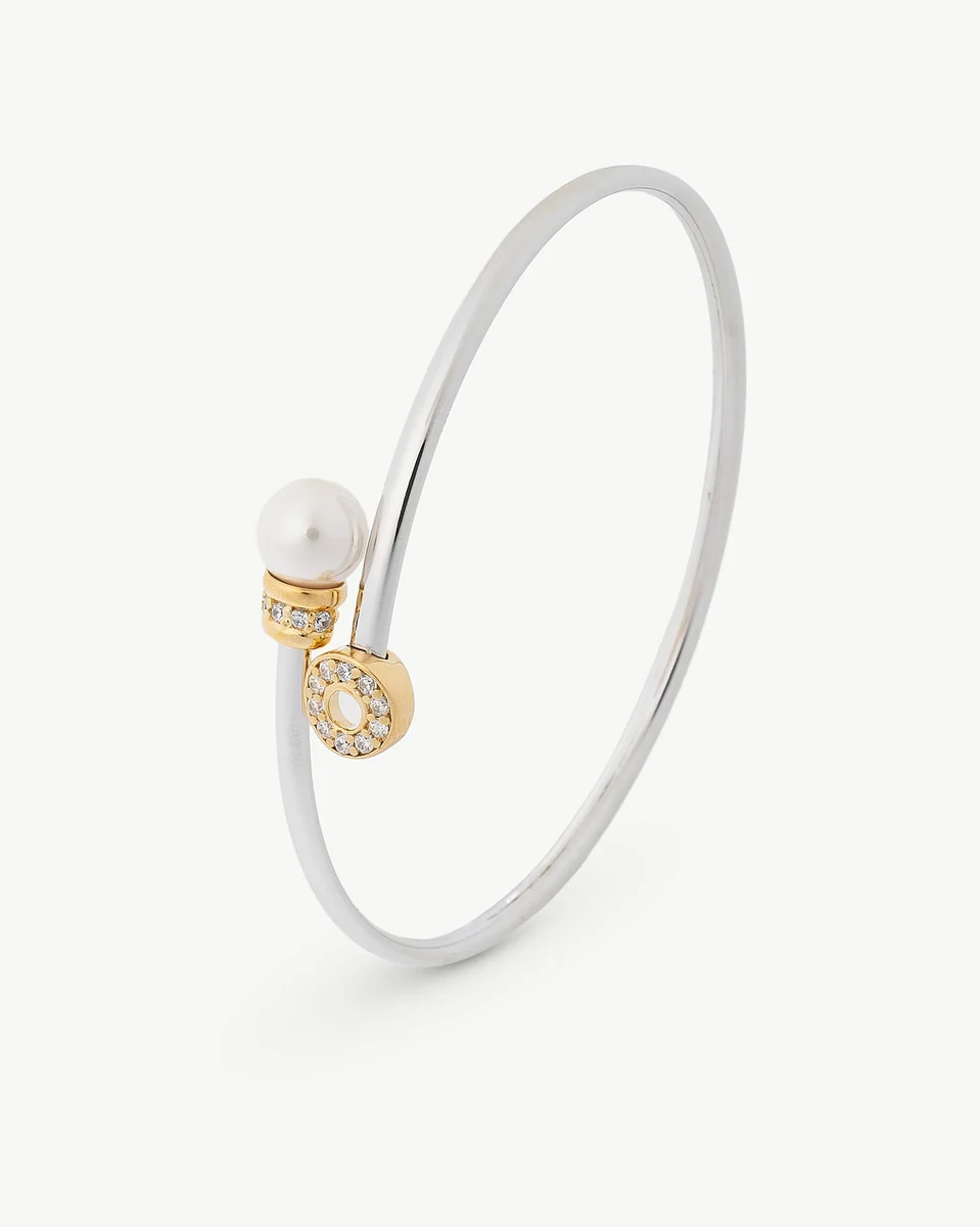 Brazalete rígido visto en ángulo lateral sobre fondo blanco, detalle de la perla y el cierre circular con circonitas.