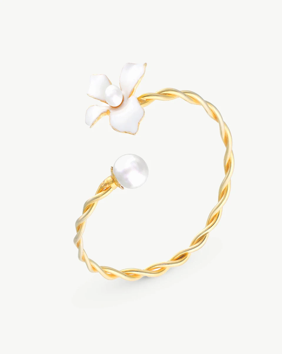 Bracelet jonc doré torsadé avec fleur émaillée blanche et perle, vue de profil sur fond blanc.