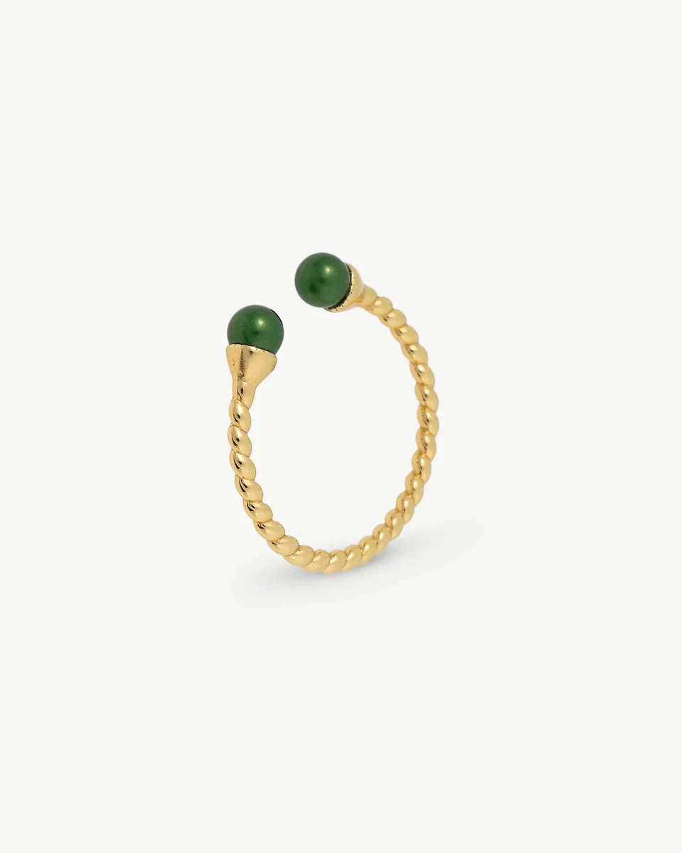 Twisted band ring with two green pearls, side angle view on a white background.