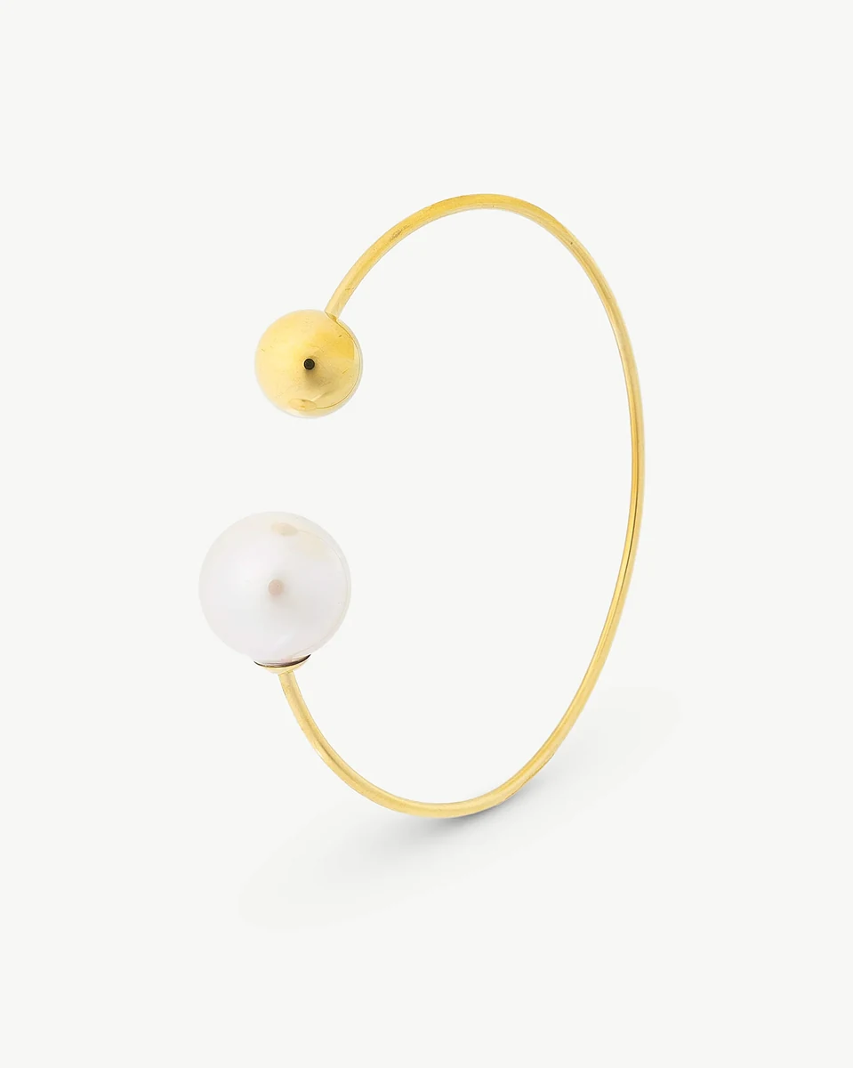 Bracelet jonc doré avec perle blanche et boule d'acier, vue de profil sur fond blanc.