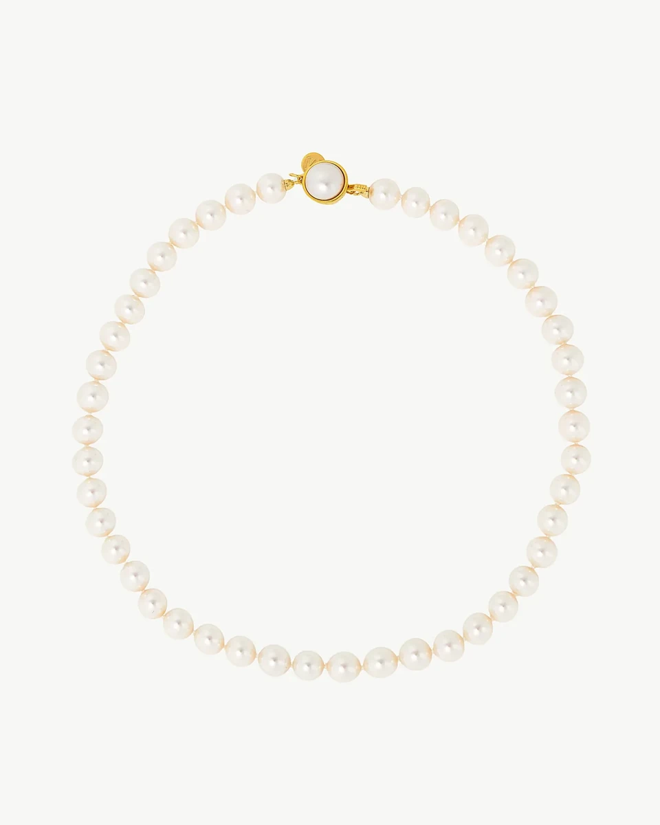 Collar de perlas dispuesto en círculo sobre fondo blanco, vista cenital con detalle del cierre dorado.