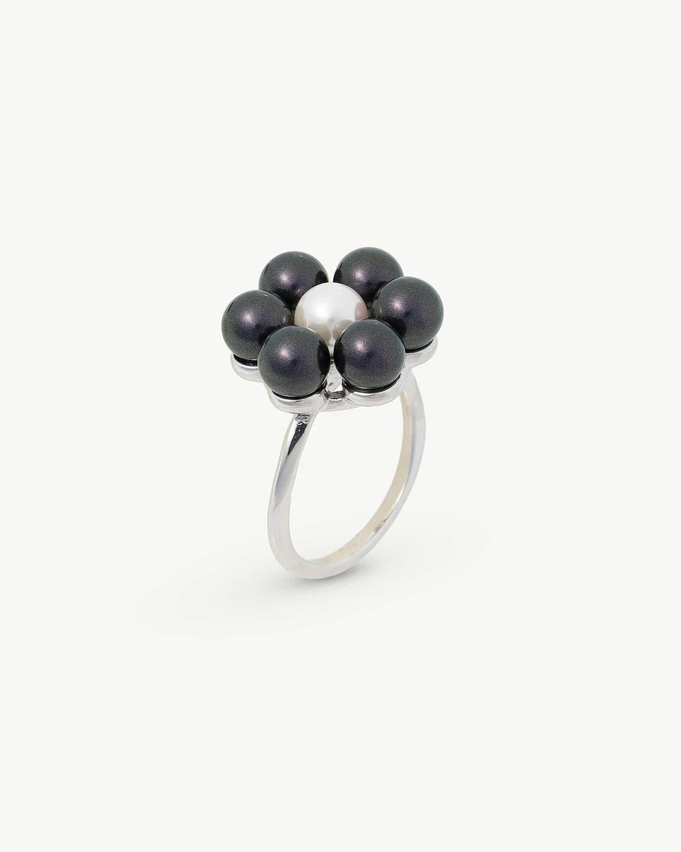 Anillo de diseño floral con perlas negras sobre fondo blanco, vista en ángulo tres cuartos.
