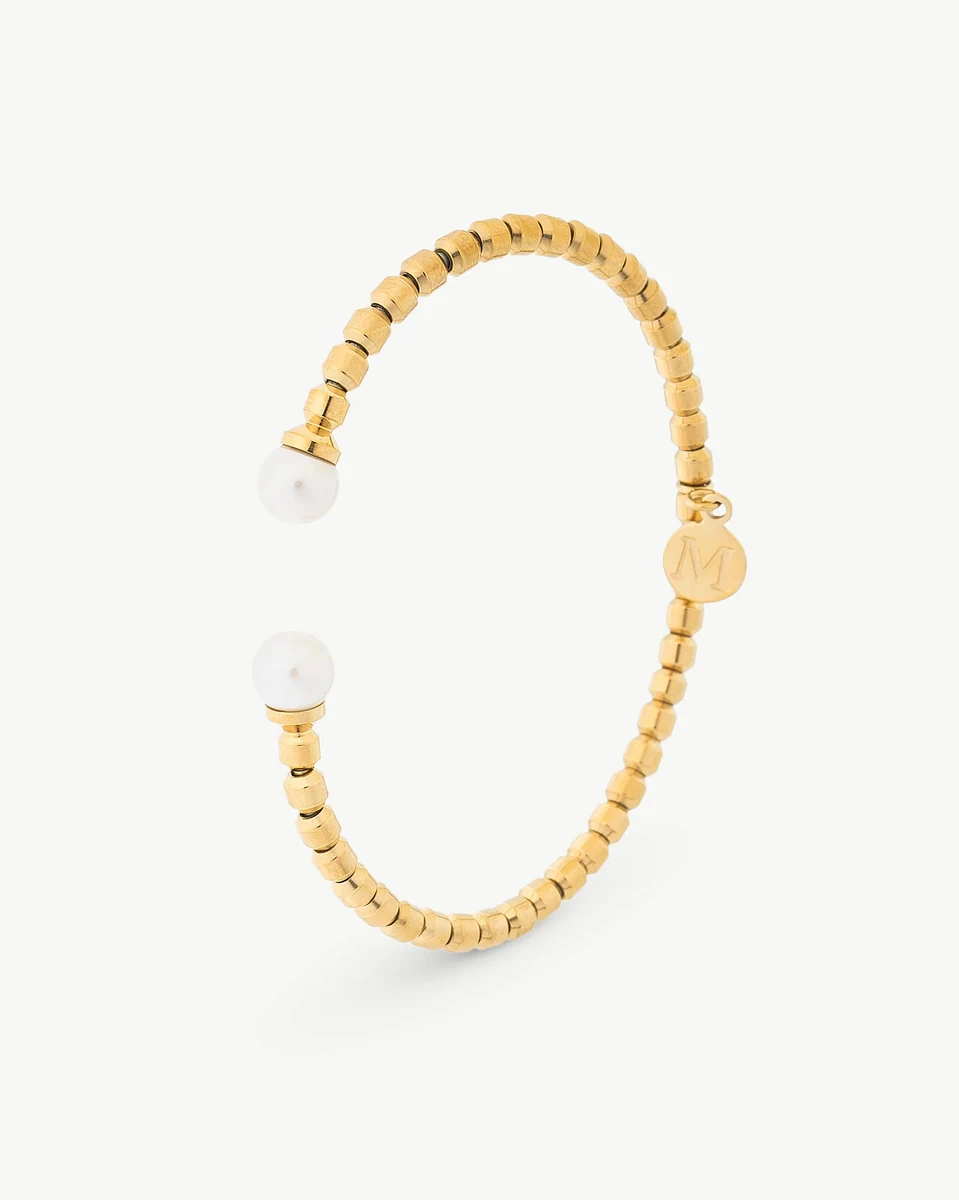 Gold rigid bangle with two white pearls, side angle view on a white background.