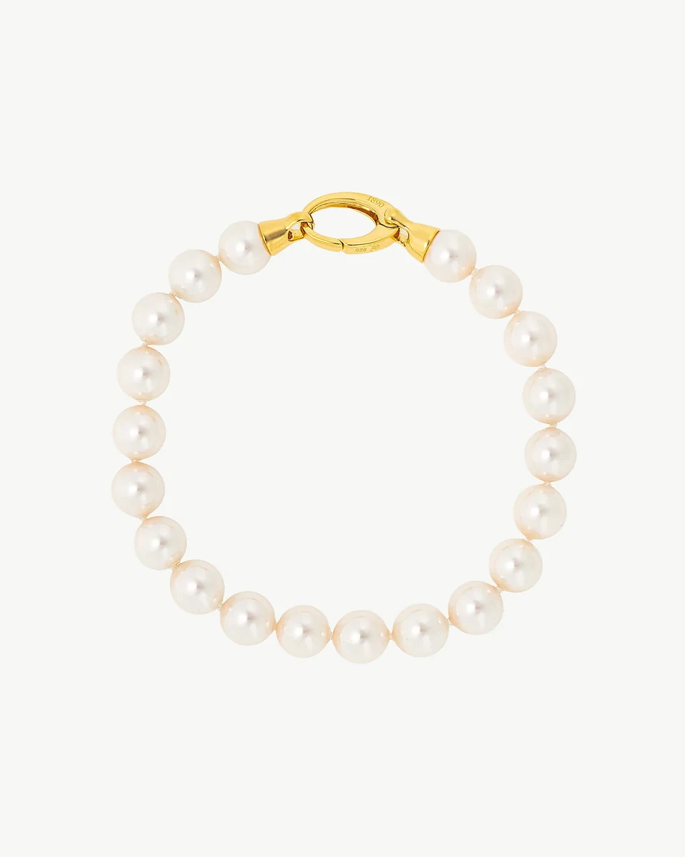 Vue de dessus d'un bracelet en perles disposé en cercle, fond blanc neutre, détail du fermoir doré.