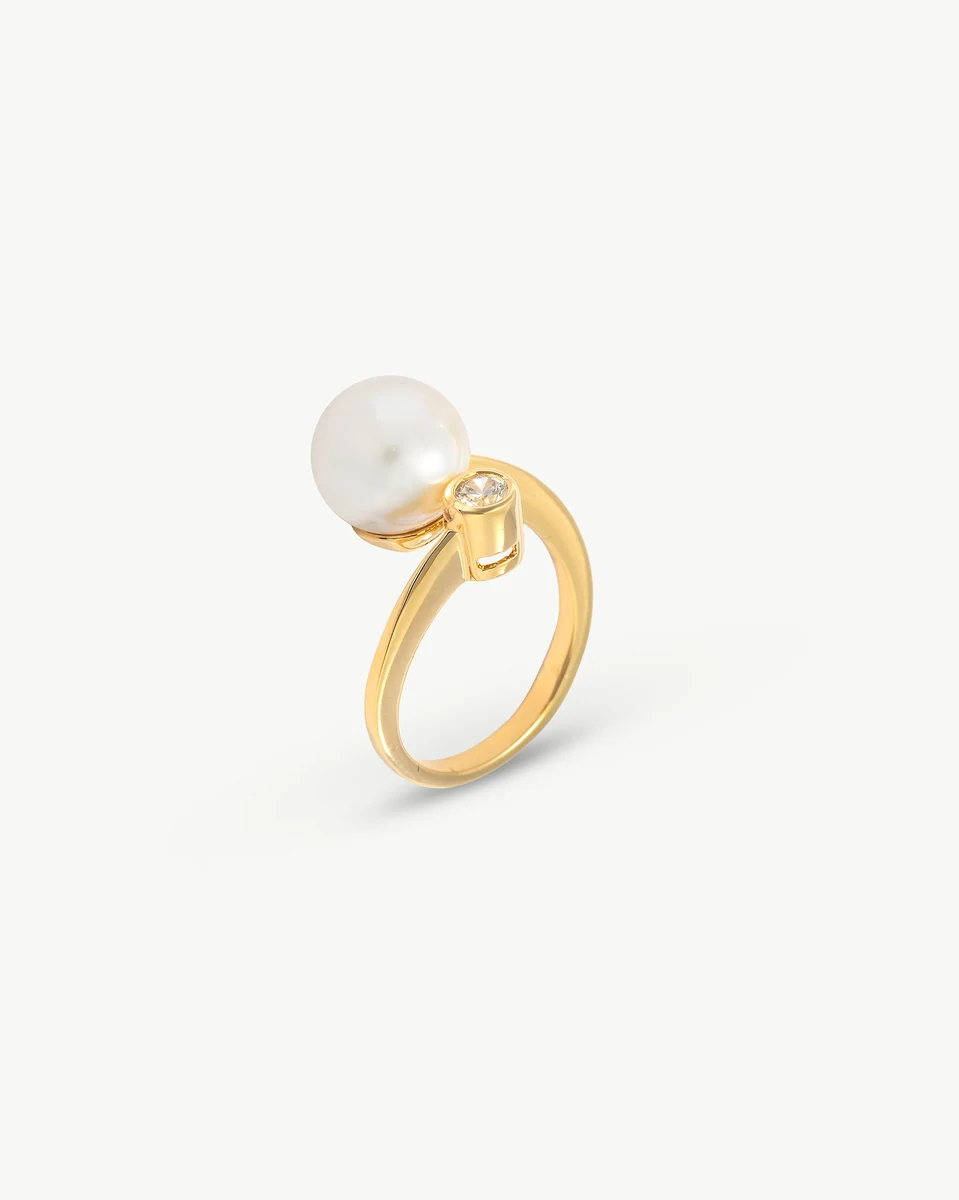 Bague perle et zircon vue de profil sur fond blanc, gros plan sur le sertissage doré.